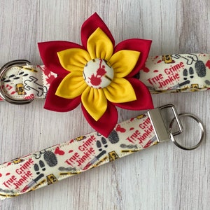 May include: A red and yellow flower with a white center is attached to a white and cream fabric dog collar with the text "True Crime Junkie". A matching fabric key chain with the same text is also shown.