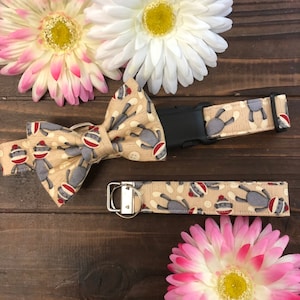 May include: A tan dog collar and matching bow tie with a pattern of monkeys wearing socks. The collar has a black plastic buckle. The bow tie and collar are on a brown wooden surface with pink flowers.