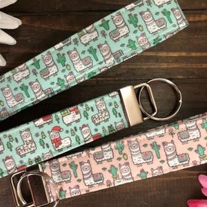 Peut inclure: Trois porte-cl&eacute;s avec un motif de lama. Les porte-cl&eacute;s sont en tissu et ont un anneau en m&eacute;tal argent&eacute;. Le motif de lama est sur un fond bleu clair avec un th&egrave;me de No&euml;l rouge et vert sur un porte-cl&eacute;s et un fond rose sur un autre porte-cl&eacute;s.