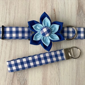 May include: Blue and white gingham dog collar with a blue and light blue flower accent. The collar has a silver buckle and a matching leash with a silver key ring.