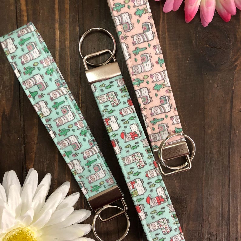 Peut inclure: Trois porte-cl&eacute;s avec des motifs de lamas. L'un est rose avec des lamas blancs, l'autre est bleu sarcelle avec des lamas blancs, et le dernier est bleu sarcelle avec des lamas blancs portant des chapeaux de P&egrave;re No&euml;l. Tous les porte-cl&eacute;s ont des anneaux de cl&eacute;s argent&eacute;s.
