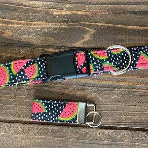 May include: A black and white dog collar with a watermelon print and white polka dots. The collar has a black plastic buckle and a silver metal D-ring. A matching key chain is also included.