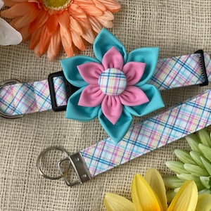 May include: A pink and blue plaid dog collar with a matching leash and a large pink and blue flower charm. The flower has a plaid center.