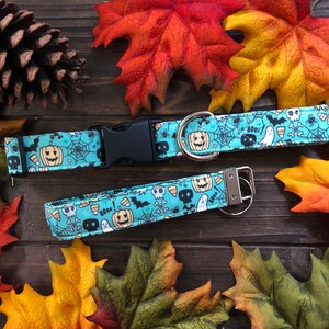 May include: A turquoise blue dog collar and matching leash with a Halloween theme. The pattern features skulls, bats, ghosts, candy corn, and pumpkins. The collar has a black plastic buckle and a silver D-ring. The leash has a silver clip.