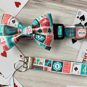 May include: A colorful dog collar and matching bow tie with a poker theme. The fabric features playing cards, poker chips, and poker terms like "Full House" and "Poker Face". A matching key chain with a similar design is also included.