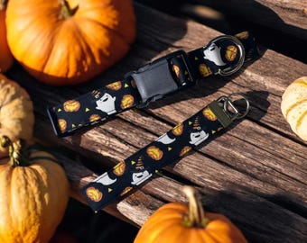 May include: A black pet collar and a matching wrist lanyard featuring a repeating pattern of white ghosts wearing orange hats and orange pumpkins. Both items include black plastic hardware and silver-toned metal D-rings for attachment.