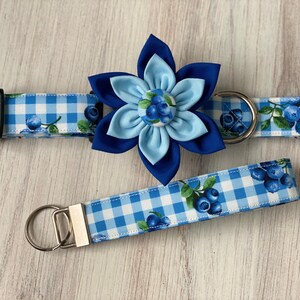 May include: Blue and white gingham dog collar with a blue flower charm and matching lead. The flower charm has a blue and white gingham centre with blue berries.