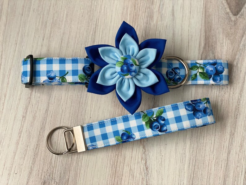 May include: Blue and white gingham dog collar with a blue flower charm and matching lead. The flower charm has a blue and white gingham centre with blue berries.