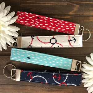 May include: Four fabric key fobs with metal hardware. The key fobs feature nautical patterns: red with white fish, white with red rope and navy anchors, light blue with white fish, and navy with red anchors and white rope.