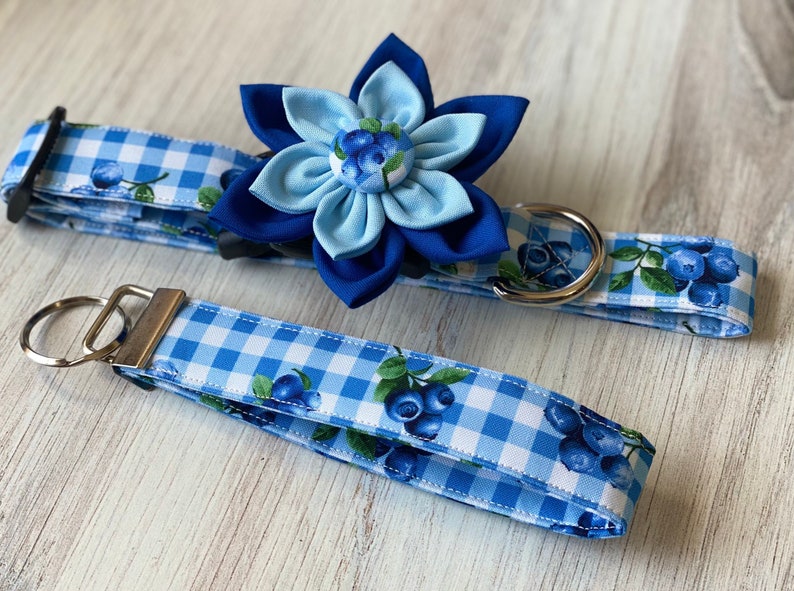 May include: A blue and white gingham dog collar with a blue flower charm and matching blue and white gingham lead with a silver key ring.