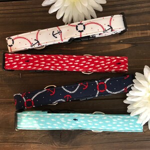 May include: Four dog collars with nautical designs. One is white with anchors and life preservers, another is red with small white fish, a third is navy blue with anchors and rope, and the last is light blue with white fish.