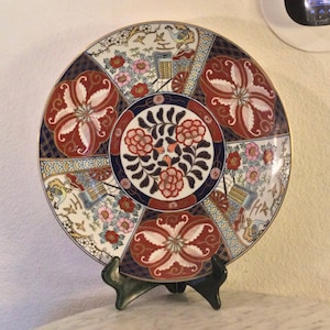 May include: A large, round, decorative plate with a gold rim. The plate features a colorful, intricate design of flowers, birds, and geometric patterns in shades of red, blue, gold, and white.