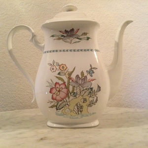 May include: White ceramic coffee pot with a floral design in shades of pink, purple, green, and yellow. The pot has a lid and a handle.
