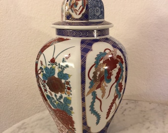 May include: A white porcelain vase with a lid, decorated with a colourful floral and bird design. The vase has a hexagonal base and a rounded body. The lid has a gold trim and a small knob on top.