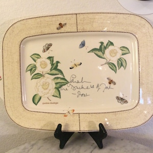 Puede incluir: Una bandeja de servir de cer&aacute;mica blanca con un dise&ntilde;o floral con camelias y mariposas. La bandeja tiene un borde marr&oacute;n y una inscripci&oacute;n manuscrita que dice "Sarah The Duchess of York - 2001".