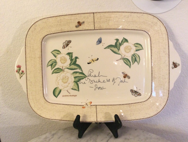 Puede incluir: Una bandeja de servir de cer&aacute;mica blanca con un dise&ntilde;o floral con camelias y mariposas. La bandeja tiene un borde marr&oacute;n y una inscripci&oacute;n manuscrita que dice "Sarah The Duchess of York - 2001".
