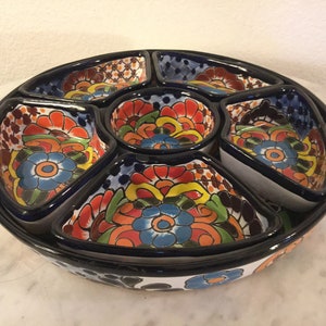 Könnte beinhalten: Eine farbenfrohe Keramik-Servierplatte mit sechs einzelnen Schalen. Die Schalen sind mit floralen Mustern in Blautönen, Rot, Gelb und Grün verziert. Die Platte ist perfekt zum Servieren von Snacks, Dips oder Vorspeisen.