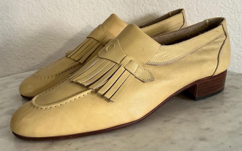 Puede incluir: Un par de mocasines de cuero amarillo claro con detalle de borlas. Los zapatos tienen un tac&oacute;n bajo y una punta redondeada. Los mocasines son un estilo cl&aacute;sico, adecuado para diversas ocasiones.