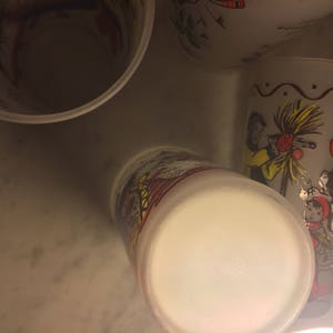 K&ouml;nnte beinhalten: Vier wei&szlig;e Keramikbecher mit bunten Illustrationen von Menschen und einem Weihnachtsbaum. Die Becher sind auf dem Kopf stehend und der Boden der Becher ist sichtbar.