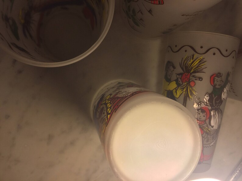 K&ouml;nnte beinhalten: Vier wei&szlig;e Keramikbecher mit bunten Illustrationen von Menschen und einem Weihnachtsbaum. Die Becher sind auf dem Kopf stehend und der Boden der Becher ist sichtbar.