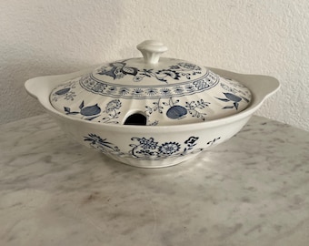 May include: A white ceramic soup tureen with a lid, featuring a blue floral pattern. The tureen has two handles and a hole for a ladle. The lid is topped with a small knob. A classic piece of serving ware.
