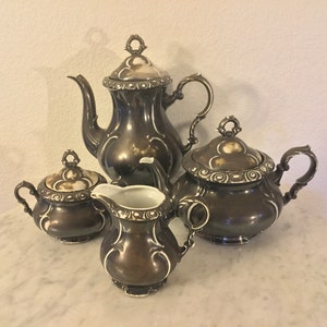 May include: A vintage silver tea set with a teapot, creamer, and two sugar bowls. The set has a brown and white floral design.