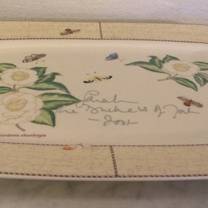 Puede incluir: Una fuente rectangular blanca con un borde decorativo que presenta un dise&ntilde;o floral con mariposas y el texto "Sarah The Mothers of Pearl - 2001".