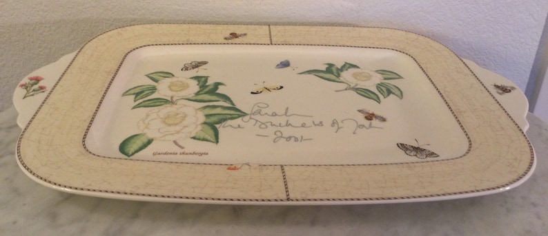 Puede incluir: Una fuente rectangular blanca con un borde decorativo que presenta un dise&ntilde;o floral con mariposas y el texto "Sarah The Mothers of Pearl - 2001".