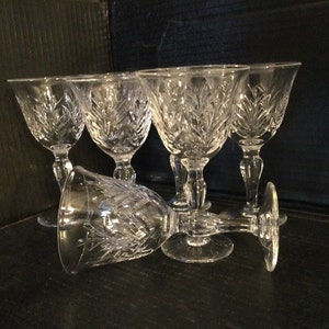 May include: Set of six clear crystal glasses with a cut design. The glasses have a round bowl and a tall stem.