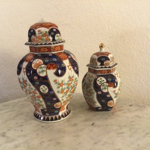 May include: Two decorative porcelain vases with intricate floral and geometric patterns in shades of blue, red, gold, and white. The larger vase is taller and wider than the smaller vase.