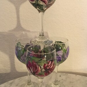Peut inclure: Ensemble de quatre verres &agrave; vin peints &agrave; la main avec des motifs floraux. Les verres pr&eacute;sentent des fleurs roses, violettes et vertes.