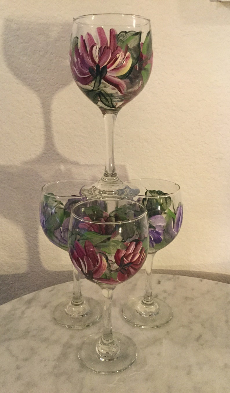 Peut inclure: Ensemble de quatre verres &agrave; vin peints &agrave; la main avec des motifs floraux. Les verres pr&eacute;sentent des fleurs roses, violettes et vertes.