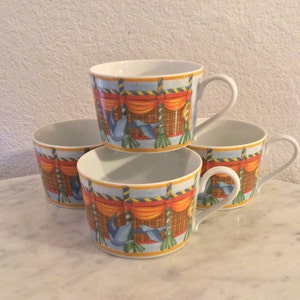 Può includere: Set di quattro tazze in ceramica bianca con un design colorato che presenta un uccello blu, tende arancioni e uno sfondo a motivi gialli e marroni.