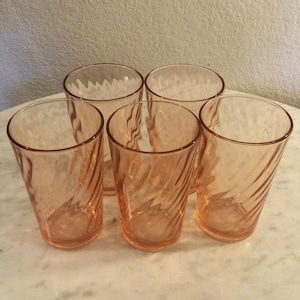 May include: Set of five pink glass tumblers with a swirl design. The glasses are clear with a pink tint and have a slightly frosted appearance.