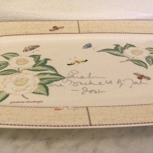 Puede incluir: Una bandeja rectangular para servir con fondo beige y borde decorativo. La bandeja presenta un dise&ntilde;o floral con camelias blancas, hojas verdes y mariposas. El texto "Each Journey is Part of the Story" est&aacute; escrito en cursiva en la bandeja.