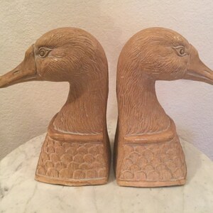 May include: A pair of brown ceramic goose bookends. The geese have detailed features and are in a standing position with their necks bent.