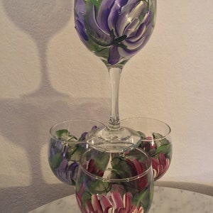 Peut inclure: Quatre verres &agrave; vin avec des motifs floraux peints &agrave; la main. Le verre du haut pr&eacute;sente une fleur violette, tandis que les trois verres du bas pr&eacute;sentent des fleurs violettes et roses.