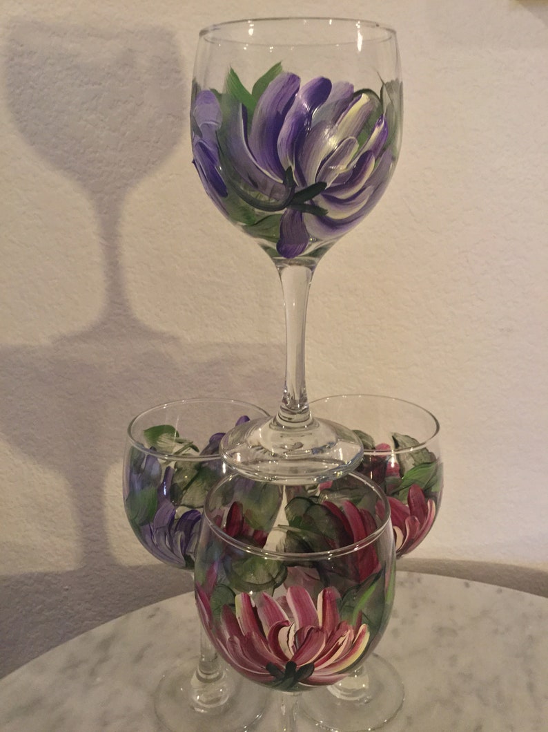 Peut inclure: Quatre verres &agrave; vin avec des motifs floraux peints &agrave; la main. Le verre du haut pr&eacute;sente une fleur violette, tandis que les trois verres du bas pr&eacute;sentent des fleurs violettes et roses.