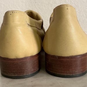 Puede incluir: Un par de zapatos de cuero de color beige claro con tacones marrones oscuros. Los zapatos tienen una punta redondeada y un tac&oacute;n bajo. El cuero parece liso y los zapatos est&aacute;n en buen estado.