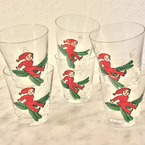 Puede incluir: Seis vasos de beber de vidrio transparente con ilustraciones rojas y verdes de duendes en ramas. Los duendes llevan gorros rojos y trajes rojos.