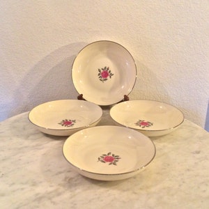 May include: Set of four white ceramic bowls with a gold rim and a pink rose design.