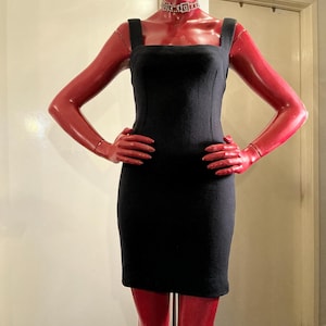 May include: A black, knee-length dress with a square neckline and thick straps. The dress is displayed on a red mannequin with arms at the sides. The mannequin is wearing a silver choker necklace.