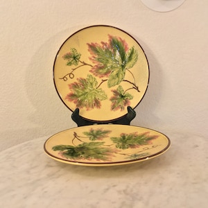 May include: Two yellow ceramic plates with a brown rim and a green and pink leaf design.