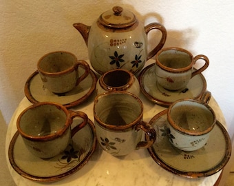 May include: A set of six ceramic teacups and saucers with a brown and gray speckled glaze. The cups and saucers have a floral design in brown, orange, and green. The set also includes a teapot with a matching design.
