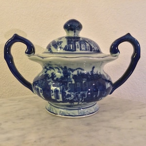 Puede incluir: Un azucarero de porcelana azul y blanco con tapa y dos asas. El tazón está decorado con un patrón floral azul y blanco.