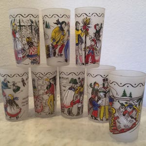 K&ouml;nnte beinhalten: Satz von acht gefrosteten Gl&auml;sern mit bunten Illustrationen von Winterszenen. Jedes Glas zeigt eine andere Szene, darunter Menschen beim Schlittschuhlaufen, einen Schneemann und eine Familie beim Schlittenfahren.