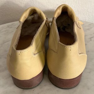 Puede incluir: Un par de zapatos de cuero amarillo claro con suelas marrones. Los zapatos tienen una punta redondeada y un tac&oacute;n bajo. El interior de los zapatos es visible, mostrando el forro y la forma del zapato. Los zapatos est&aacute;n en buen estado.