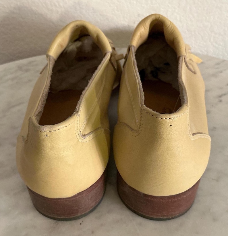Puede incluir: Un par de zapatos de cuero amarillo claro con suelas marrones. Los zapatos tienen una punta redondeada y un tac&oacute;n bajo. El interior de los zapatos es visible, mostrando el forro y la forma del zapato. Los zapatos est&aacute;n en buen estado.
