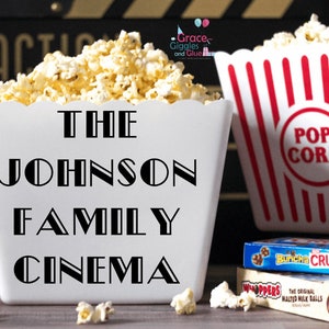 May include: White popcorn bucket with black text that reads "The Johnson Family Cinema". The bucket is filled with popcorn and is next to a red and white striped popcorn bucket that says "Pop Corn".
