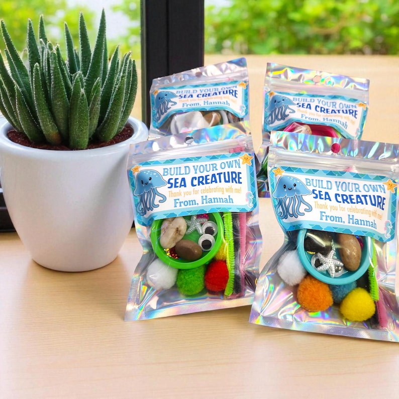 May include: Several clear cellophane bags filled with craft supplies for creating sea creatures. Each bag has a label that reads "Build Your Own Sea Creature" and includes a variety of colorful pom-poms, pipe cleaners, and googly eyes.